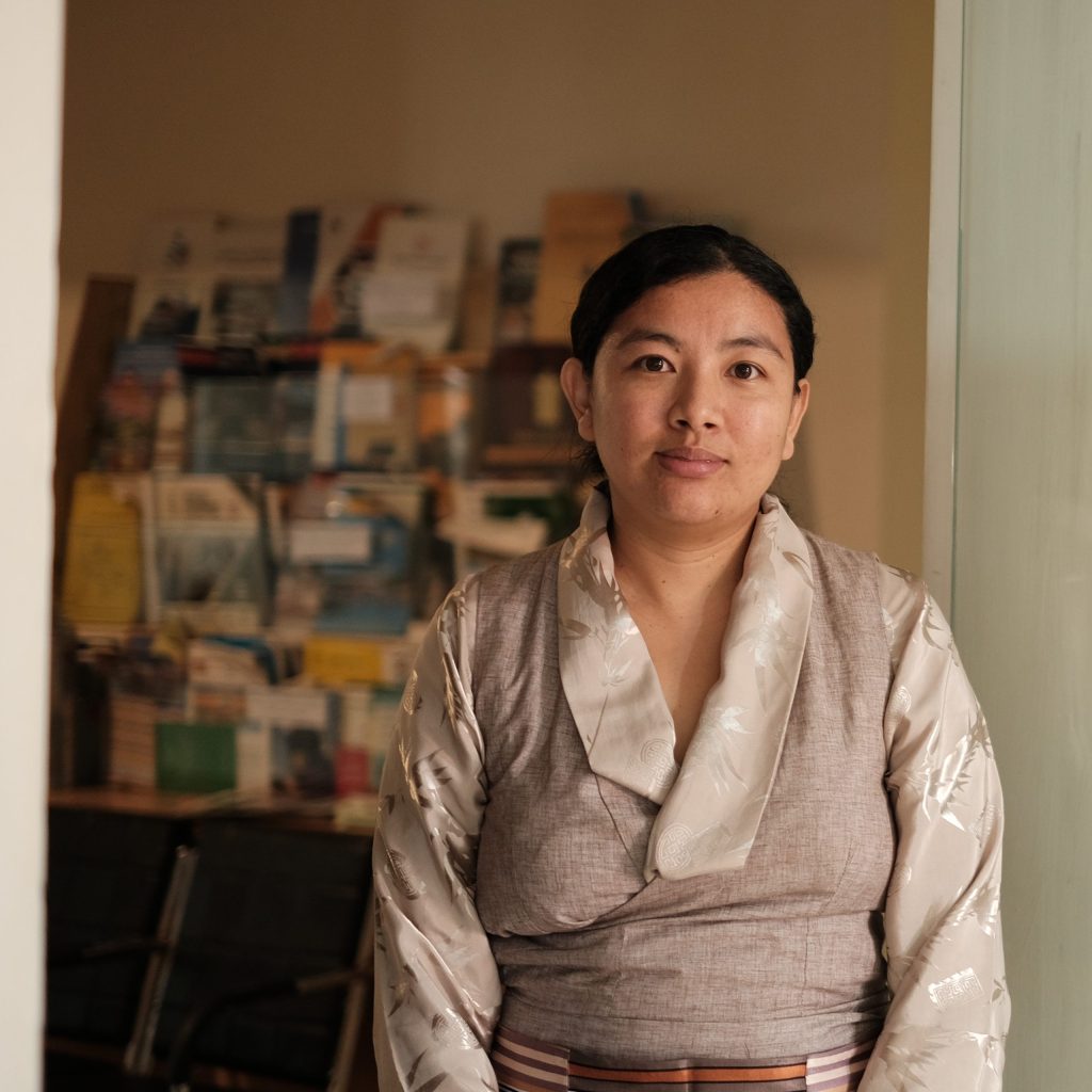 Person in a light kimono standing in a doorway, with a blurred room behind them.