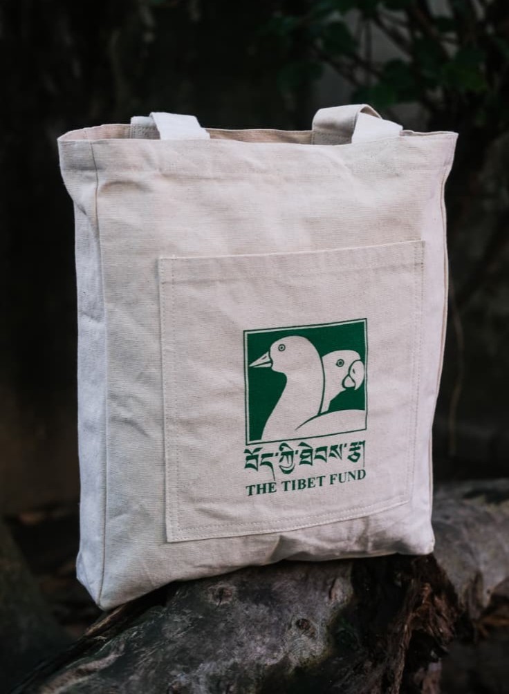 Beige canvas tote bag with The Tibet Fund logo: two white ducks on a green square surface on the front pocket.