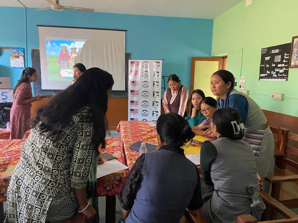 Group of adults in a classroom attending a workshop, near a projector screen showing a rural photo