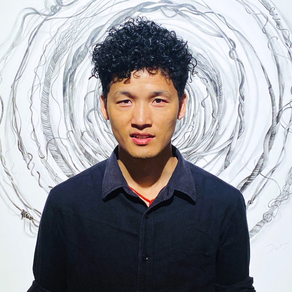Man with short curly black hair wearing a dark shirt, photographed from chest up against a light background with swirling gray vines behind him.