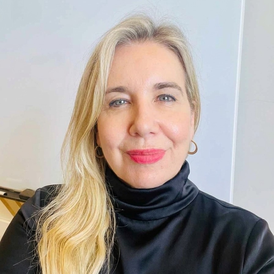 Smiling woman with blonde hair wearing a black turtleneck, facing the camera in a neutral setting.