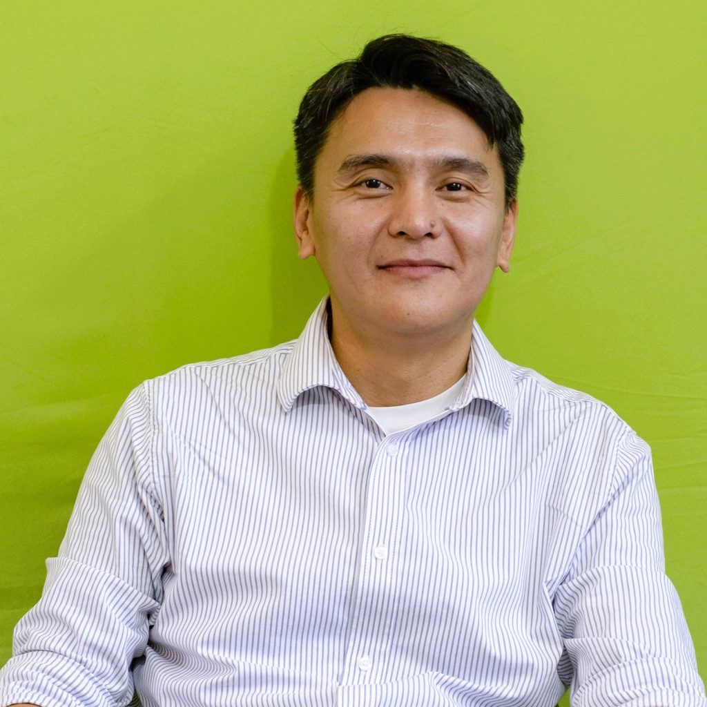 Smiling man with short black hair in a striped shirt, posed against a bright lime green background.